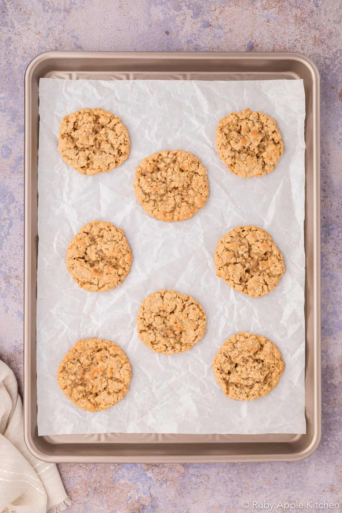 Freshly baked oatmeal cookies cooling on a parchment-lined baking sheet.