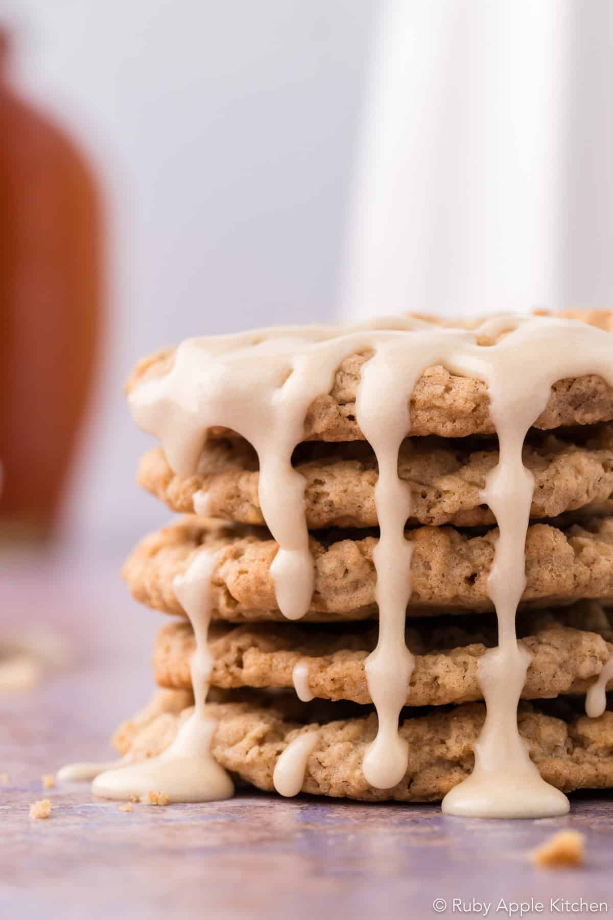 Cream-colored maple glaze dripping down the sides of a stack of oatmeal cookies.