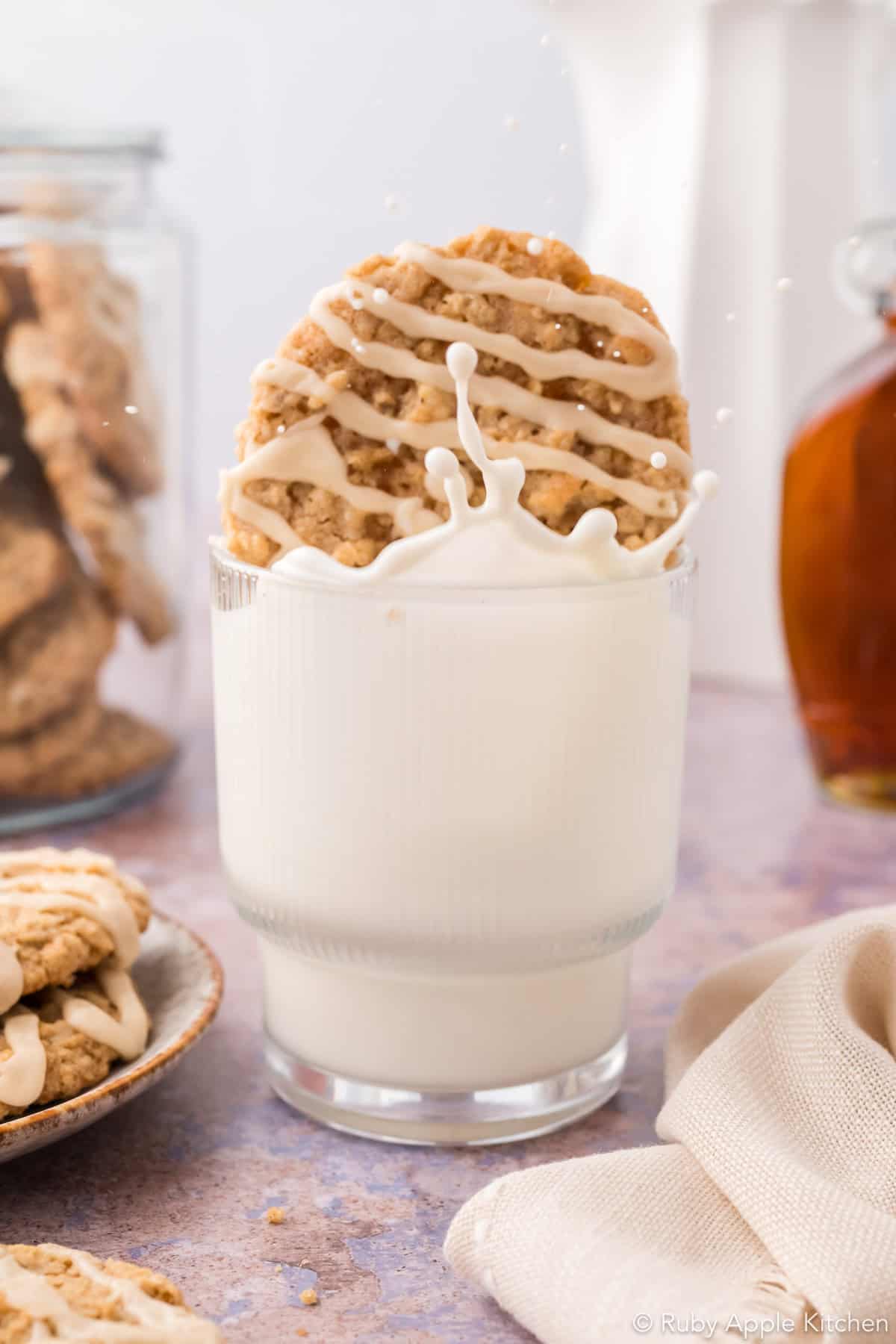 Maple oatmeal cookie dunked into a glass of milk, sending milk splashing above the rim.