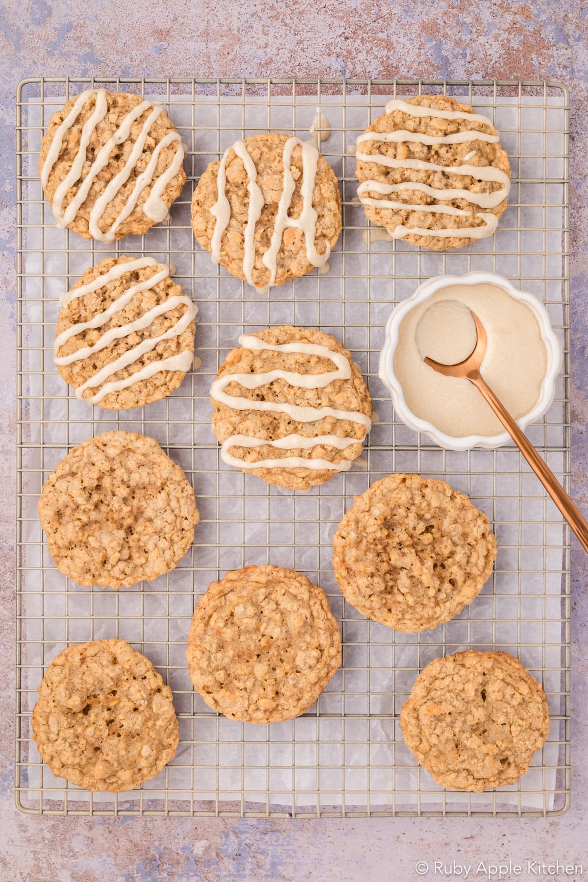 Plain and maple-glazed oatmeal cookies side by side on a cooling rack, with a bowl of glaze nearby.