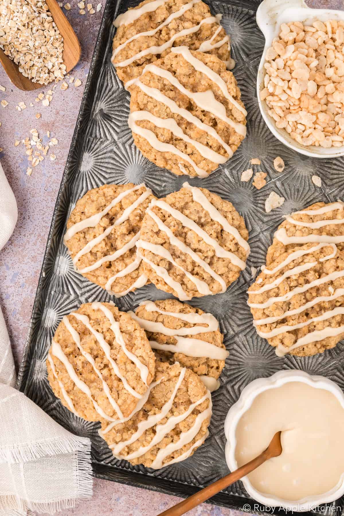Overhead view of maple oatmeal cookies topped with cream-colored maple glaze on a metal tray.